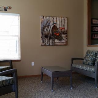 A cozy living room featuring two chairs, a small table, a window, and wall art.