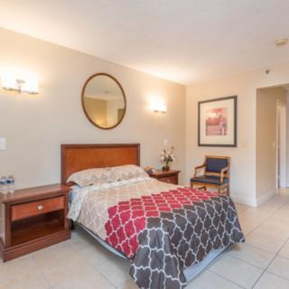 A cozy bedroom featuring a bed with a patterned blanket, nightstand, wall decor and lighting fixtures.