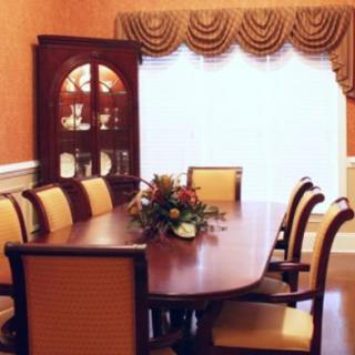 Elegant dining room with a polished wooden table and upholstered chairs, complemented by decorative curtains and a floral centerpiece.