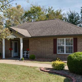 A cozy single-story brick house with a well-maintained front yard and surrounding trees.