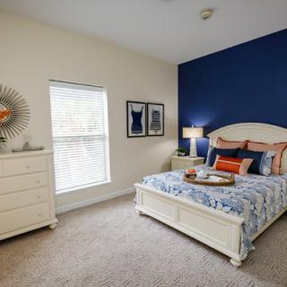 A stylish bedroom with a blue accent wall, featuring a bed, dresser, and modern decor.