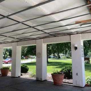 A view of a carport featuring potted plants and a lush green landscape.