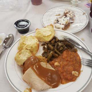 A hearty meal featuring turkey with gravy, green beans, a bread roll, and a sweet dessert.