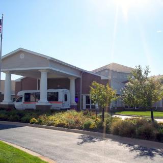 A modern building with a covered entrance, surrounded by landscaping and a driveway under a clear sky.