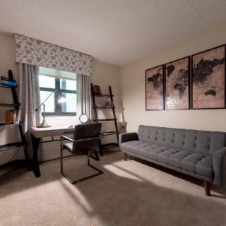 A cozy home office with a desk, chair, and sofa, featuring map-themed wall art.