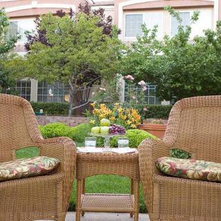 A cozy outdoor garden setting with wicker chairs and a small table adorned with colorful flowers.