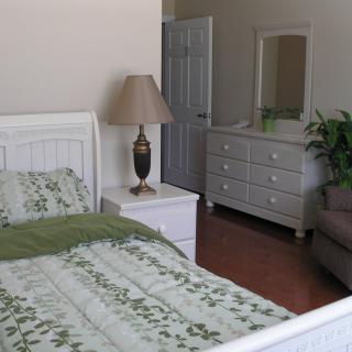 A cozy bedroom with a bed, nightstand, lamp, dresser, and mirror.