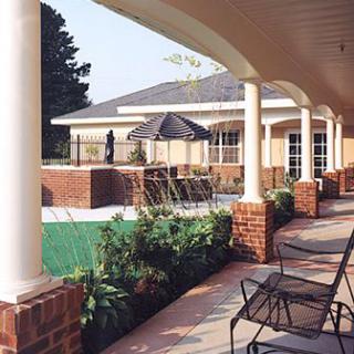 A covered patio area with chairs and columns overlooking a garden.