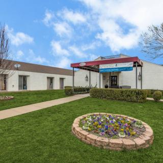 A building with a landscaped entrance featuring a flower bed and a green lawn on a sunny day.