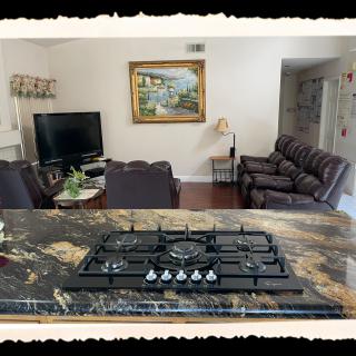 A view from the kitchen into a cozy living room with a TV, sofas, and artwork on the wall.
