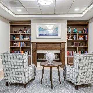 A cozy reading nook with armchairs facing a small table and globe, surrounded by bookshelves filled with various books and decor.