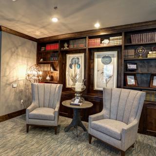 A cozy library corner with two elegant chairs, a small table, and well-stocked bookshelves.