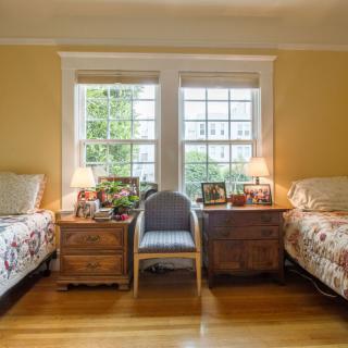 A cozy bedroom with twin beds, warm lighting, and large windows.