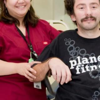 Two people smiling indoors, with one wearing a Planet Fitness shirt.