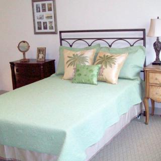 A neatly arranged bedroom with a pastel green bedspread and decorative pillows.