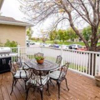 A cozy patio deck with a table, chairs, and a grill overlooking a neighborhood street.