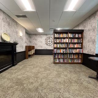 A spacious and elegantly designed reading area featuring bookshelves filled with books, complemented by stylish wallpaper and carpet.