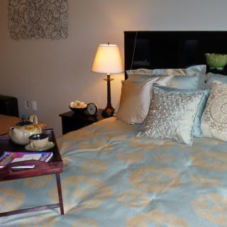 A cozy bedroom with elegant bedding and a bedside lamp, featuring decorative pillows and a serving tray.