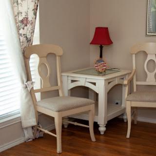 A cozy corner featuring two beige chairs and a white side table with a red lamp.
