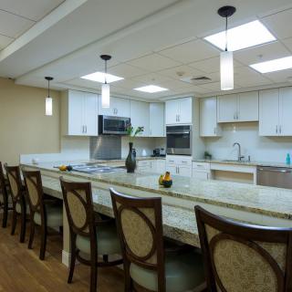 A spacious modern kitchen with a long countertop, surrounded by chairs and illuminated by pendant lights.