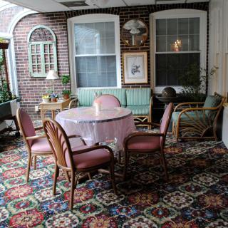 A cozy seating area with a table and chairs, featuring a decorative carpet and large windows.