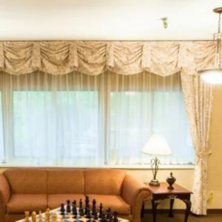 A cozy living room featuring a chess board on the table, with elegant curtains and a comfortable sofa.
