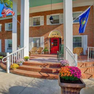 The image shows a building entrance with large columns, flags, and colorful flowers on the steps.