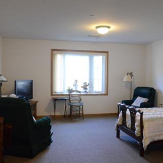 A cozy room with a bed, chair, television, and a window.