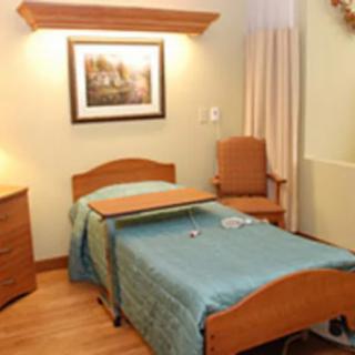 A hospital room with a single bed, bedside table, and a framed picture on the wall.