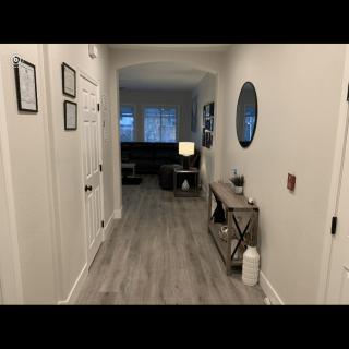 A well-decorated hallway in a home featuring light wood flooring, wall art, and a console table with a round mirror above it.