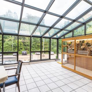A modern conservatory with a glass roof, offering ample natural light and views of lush greenery, featuring a dining area.