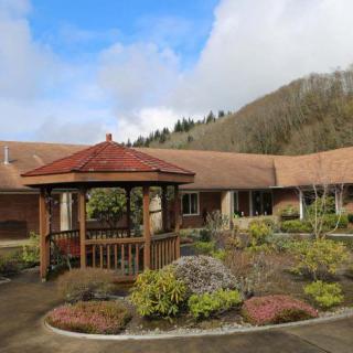 A peaceful courtyard featuring a wooden gazebo surrounded by landscaped gardens and a building in the background.