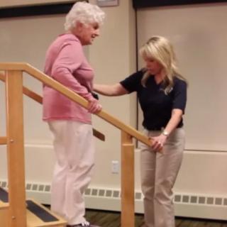 A healthcare professional assisting an elderly woman with physical therapy exercises on the stairs.