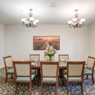 A well-lit dining room with a long table, surrounded by chairs and decorated with flowers and artwork.
