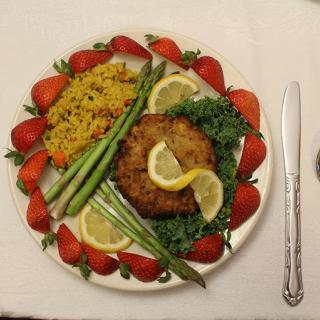 A beautifully arranged meal featuring a fried patty, asparagus, lemon slices, rice, and strawberries.