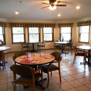 A cozy dining room with round tables and chairs, featuring large windows and a ceiling fan.