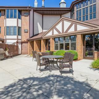 A sunny outdoor patio area with tables and chairs in front of a brick building.