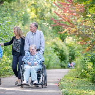 A family enjoying a walk in the park, with one member in a wheelchair, surrounded by lush greenery.
