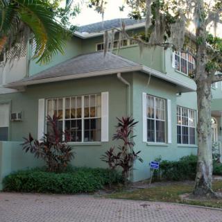 A green residential house surrounded by trees and landscaping.