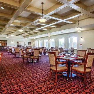 A spacious dining room with elegantly arranged tables and chairs, featuring large windows and decorative ceiling lights.