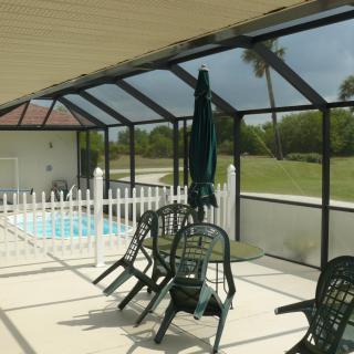 A screened-in patio with poolside furniture and a view of the outdoors.