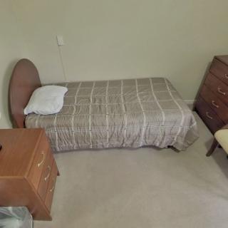 A simple bedroom with a single bed, dresser, and nightstand.
