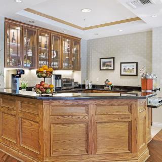 A cozy kitchen bar area with wooden cabinetry and a granite countertop, featuring appliances and fruit arrangements.