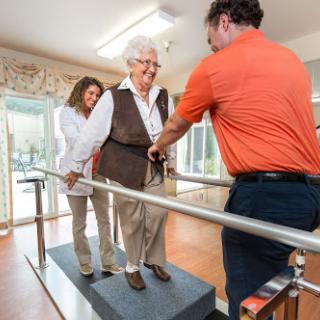 A physical therapist assists an elderly woman in walking using a supportive railing system.