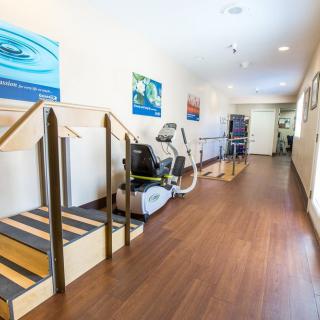 A well-equipped physical therapy room featuring exercise machines, stairs, and parallel bars.