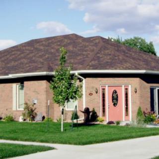 A suburban brick house with a well-kept lawn and a small tree in the front yard.