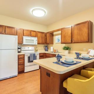 A modern kitchen with wooden cabinets, equipped with appliances and a small dining area.