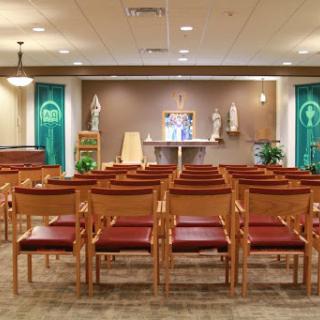 A serene interior of a chapel, featuring rows of wooden chairs facing an altar adorned with decorations and green banners.