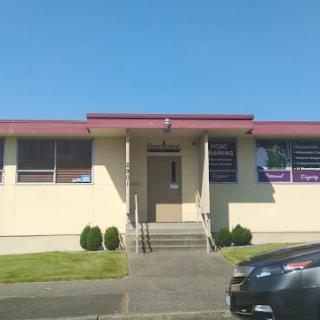 A small building with an entrance and steps, featuring signs on the windows, and a car parked nearby on a sunny day.