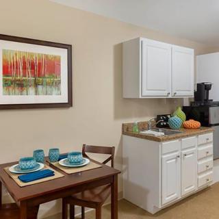 A cozy kitchen and dining area featuring a small table set for two, white cabinets, and colorful artwork on the wall.